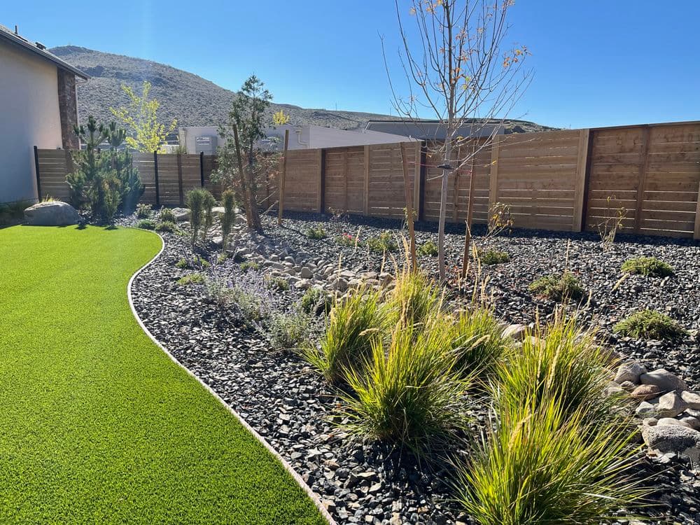 Lush green lawn landscape design with stone features and shrubs under clear blue sky.