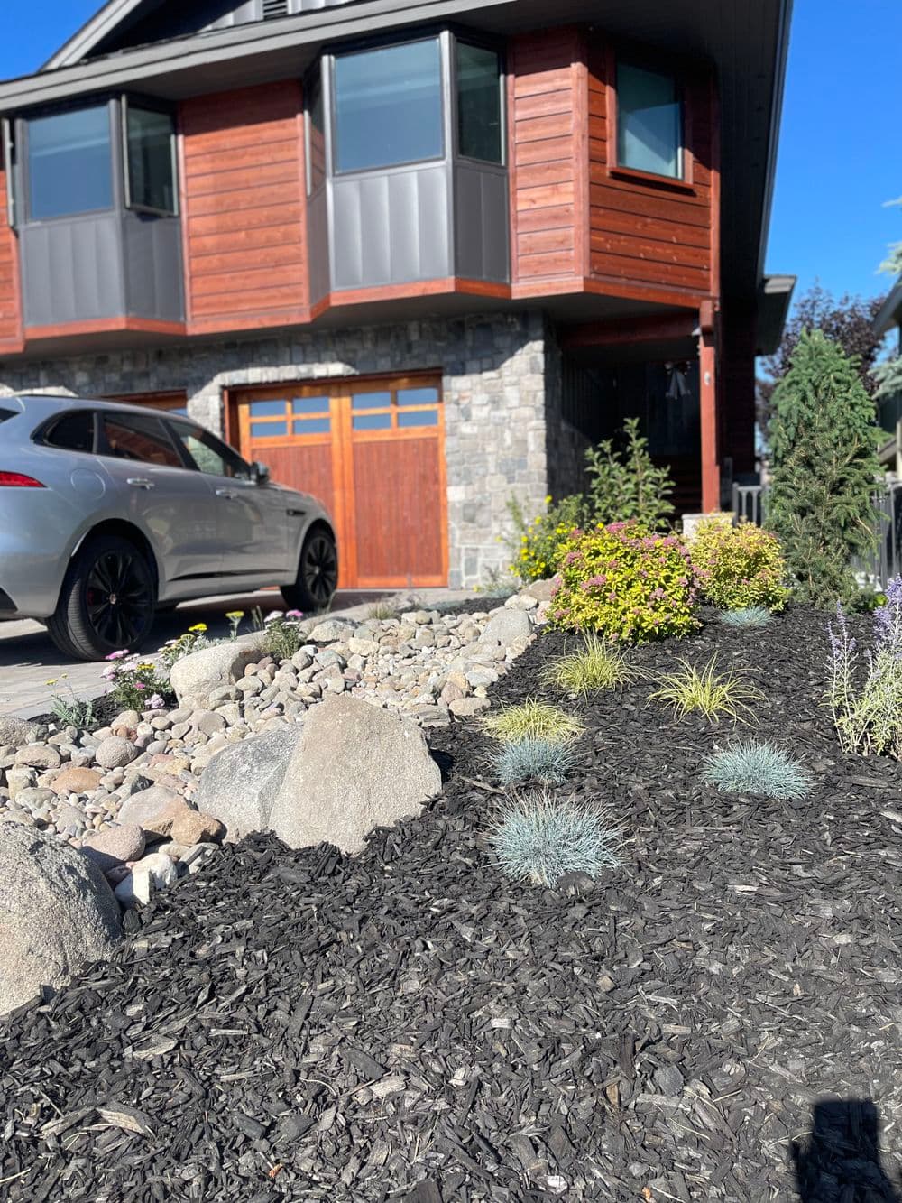 Modern home exterior with landscaped garden featuring rocks, mulch, and colorful shrubs.