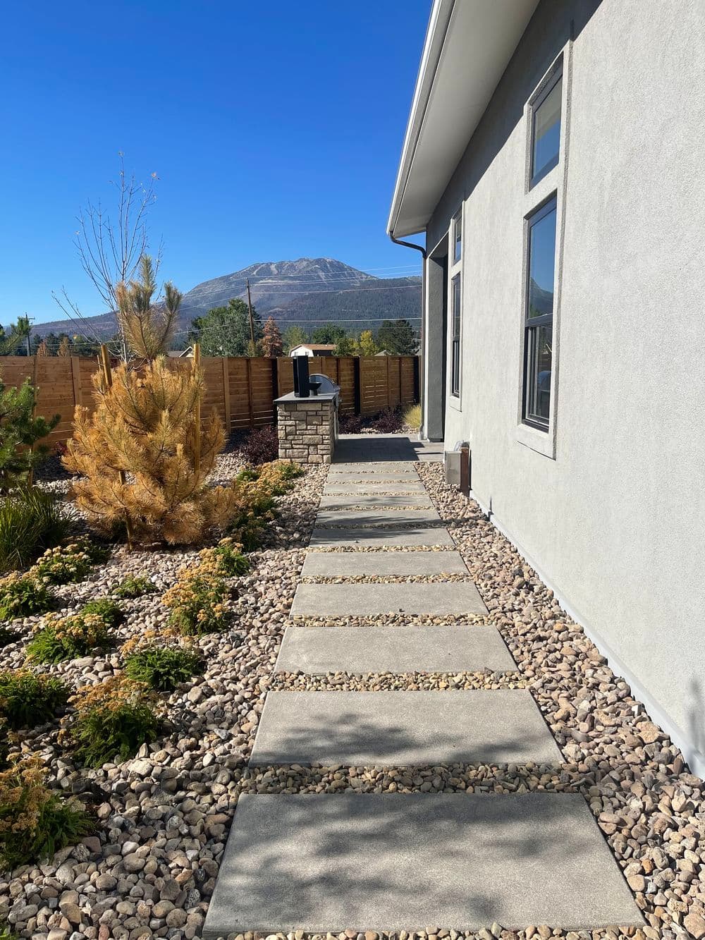 Pathway leading to a modern house, surrounded by landscaped stones and mountains in the background.